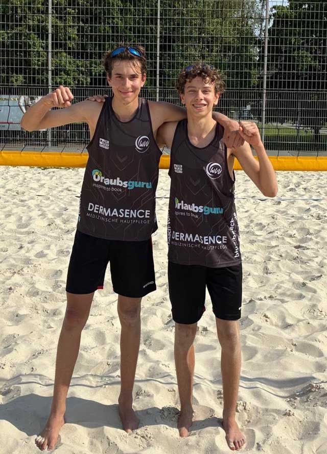 Anton und Dario stehen in Siegerpose auf dem Beachvolleyballfeld vor dem Netz